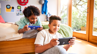 Two kids play together on their own Nintendo Switch Lite systems.